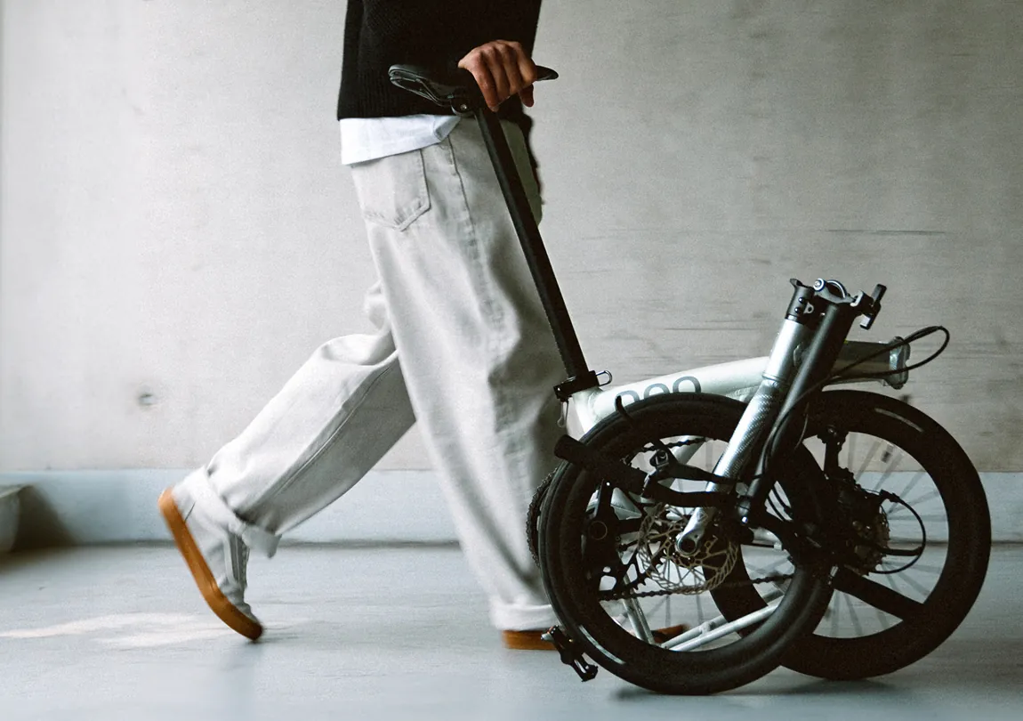 The same rider wheeling a folded white Java Neo 3 past a concrete wall
