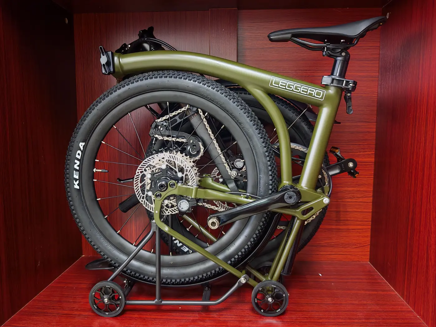 A matte green Leggero Explorer GS with Kenda off-road tyres, folded in a red wooden display cubby