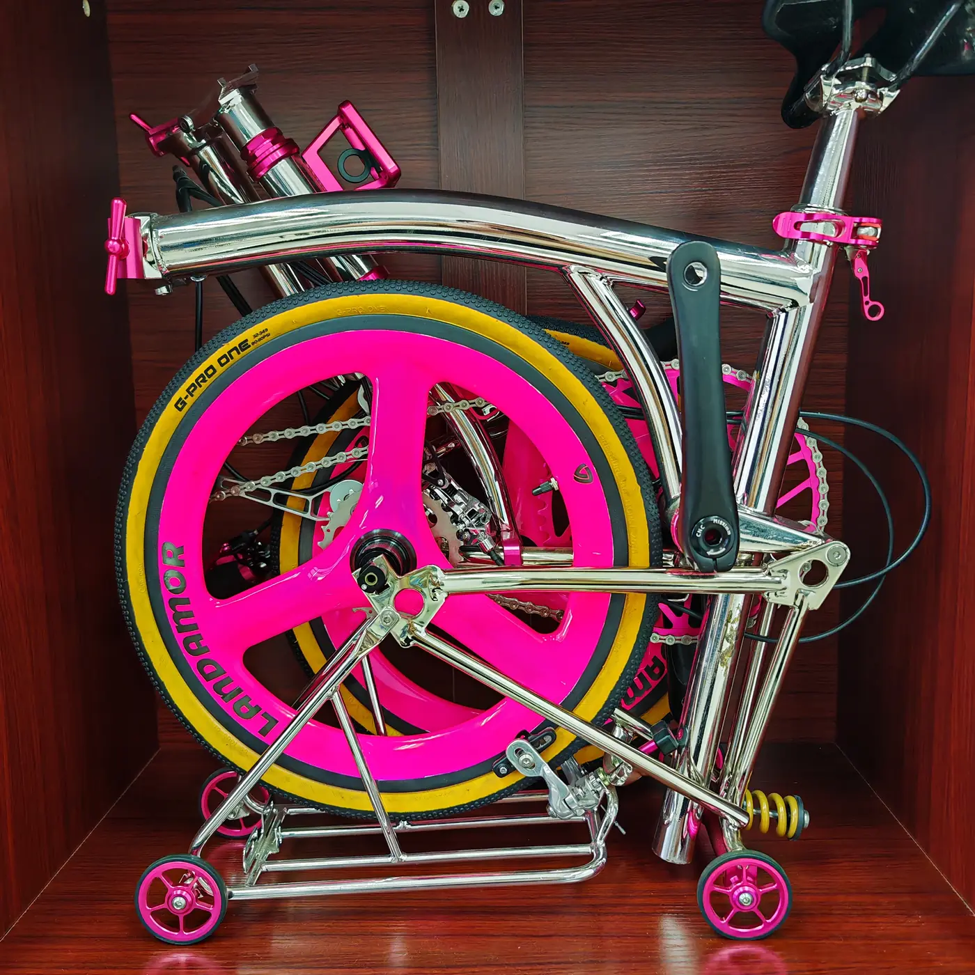 A chrome titanium 16-inch trifold with hot pink tri-spoke wheels and pink parts, folded in a red display cubby