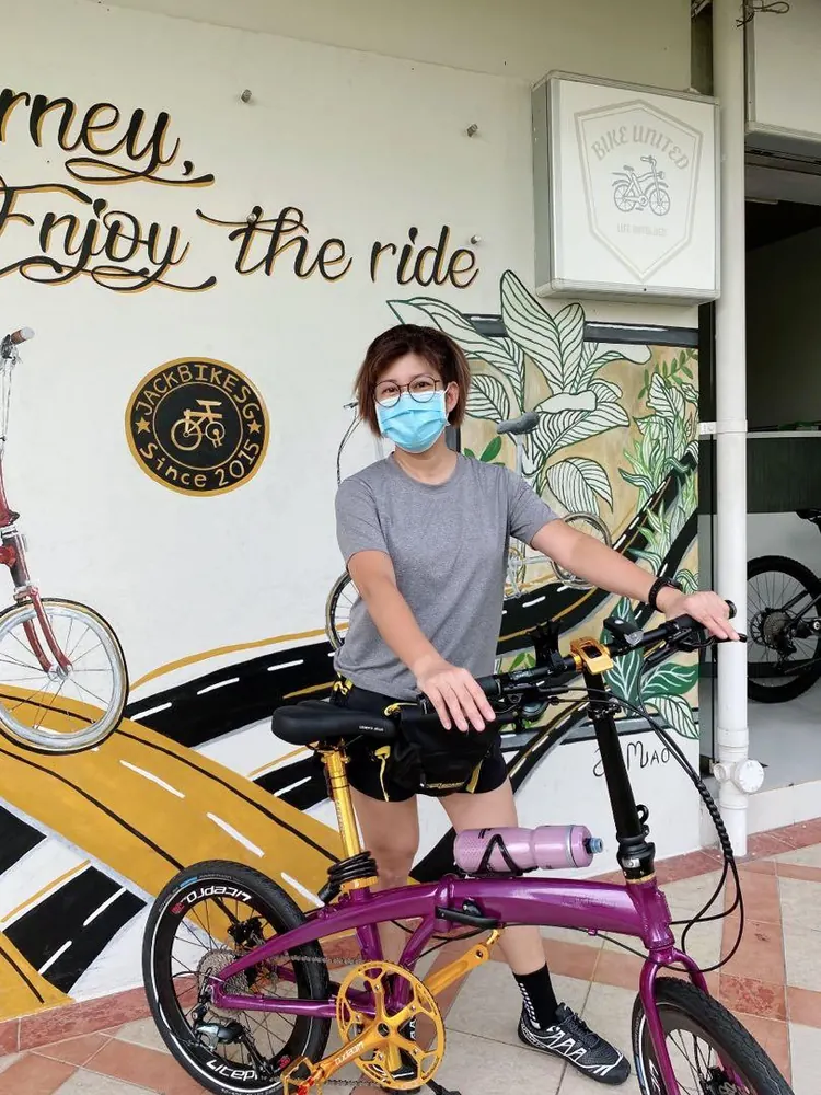 A rider with her purple and gold custom folding bike in front of a mural reading Enjoy the ride