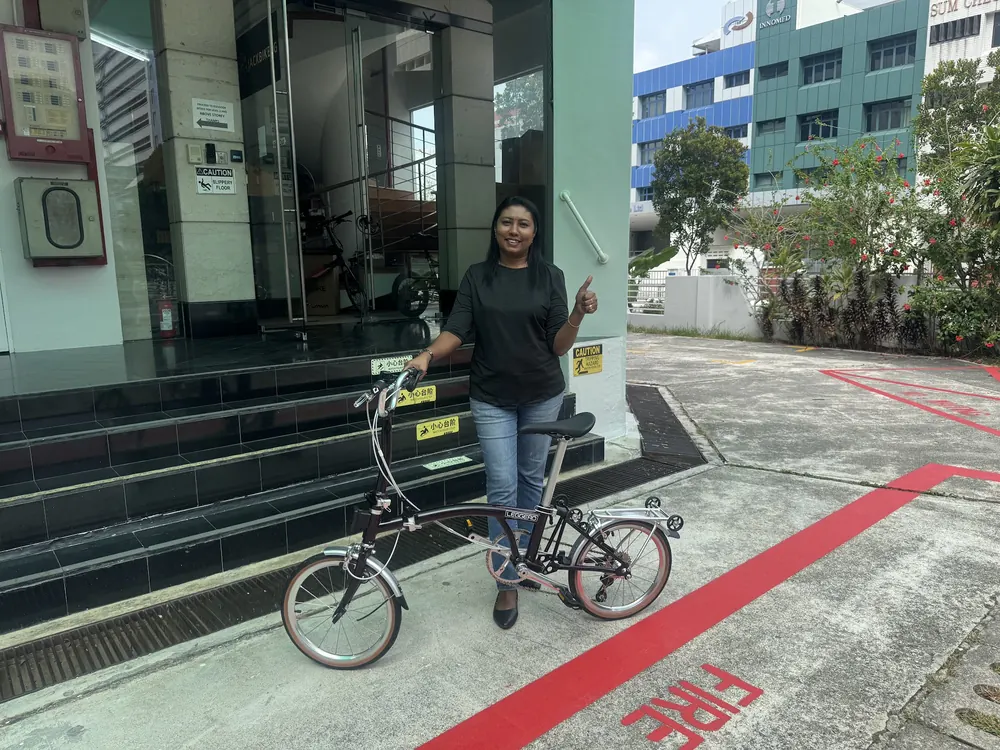 A woman giving a thumbs-up beside her new folding bike outside AZ @ Paya Lebar